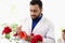 Botanist scientist in hold chemical extraction glass flask standing near red rose flower, biological researcher man do science