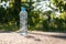 Bottle with clean cool water stands on the asphalt road in a summer hot day in the sun on a blurred background.