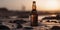 bottle of cold beer on the sand of the beach at sunset, alcoholic drink in sun backlight at a beautiful sunrise, generative AI