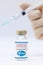 Bottle of coronavirus vaccine with the Pfizer logo and dr hands with syringe background.