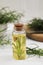 Bottle of essential oil and fresh tarragon leaves on white wooden table