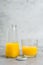 Bottle and glass with yellow liquid juice halthy beverage on gray concrete background. Orange fresh