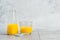 Bottle and glass with yellow liquid juice halthy beverage on gray concrete background. Orange fresh