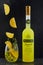 A bottle of Italian alcoholic liquor Limoncello, a glass with ice and a drink into which slices of lemon fall on a black