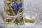 A bottle of lavender tincture. A bouquet of lavender is tied to the bottle. Nearby is a glass of drink. On coarse linen. Close-up