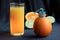 A bottle made of natural orange with a drinking tube and a glass of freshly squeezed orange juice surrounded by slices of tropical