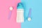 Bottle of milk for newborn baby and spoon with powdered infant formula on light pink blue table background