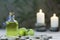 bottle of oil massage, river pebbles, two small green apples and two lighted candles on wooden table and herbal background