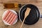 Bottle of oil, peeled sausages in plate, food turner in frying pan on wooden table. Top view