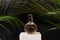 Bottle of perfume on wood podium with palm green leaves on black background. perfumery and fresh scent concept