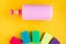 Bottle with pink dishwashing liquid and multicolor sponges on bright yellow background.