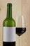Bottle of red wine with a brilliant glass on a wooden background