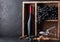 Bottle of red wine and empty glasses with dark grapes inside vintage wooden box on black stone background. Corks and corkscrew on