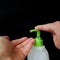 Bottle sanitizer with green dispenser with drop of disinfectant and one human palm is open, other presses the dispenser