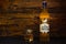 A bottle of The Snow Grouse Scotch Whisky and a glass of ice on a dark wooden background. The whiskey is based on cold