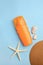 Bottle of sunscreen, starfish and seashells on light blue background, flat lay