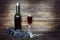 Bottle and transparent wineglass with red wine and bunch of grapes on brown wooden plank surface, corkscrew nearby