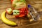 Bottle of water, apple, banana and lunch box with sandwiches and fresh vegetables on wooden table