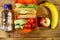 Bottle of water, apple, banana and lunch box with sandwiches and fresh vegetables on wooden table. Top view