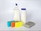 Bottle with white dishwashing liquid, scouring powder and four foam sponges of different colours on a white background.