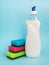 Bottle with white dishwashing liquid and three foam sponges of different colours on a blue background. Kitchen detergent.