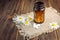 Bottle of white herbal pills and chamomile flowers on dark wooden background, homeopathic medicine