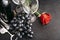 Bottle of wine, 2 empty glasses, bunch of dark grapes, red rose flower, corkscrew on a black background, top view