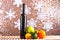 Bottle of wine and fruits on wooden surface, shimmering background with snowflakes. Fruits as orange, apple and avocado