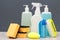 Bottles of dishwashing liquid, brushes and sponges on gray background