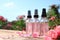 Bottles of facial toner with essential oil and fresh roses on wooden table against blurred background