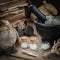 Bottles of homeopathic globules, mortar, dried moss, old books, dry roots, nuts and plants on table.