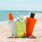 Bottles of sun protection lotion, aloe soothing gel from sun burn, seashells in sand on the beach with sparkling sea in