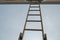 Bottom-up view of composite ladder leaning against wall of house, resting under wooden door to attic under roof trim.