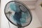 A bottom up wide angle view of a black floor standing electric fan with blue fan blades in a bedroom