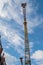 Bottom view of boom of yellow tower crane with frame ties along entire length of mast and jib with cabin on cloudy sky.