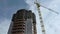 Bottom view of high building unfinished construction near the yellow crane on blue, cloudy sky background. High rise