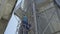 Bottom view of male Caucasian worker climbing up the ladder on huge metal tower. Confident professional man in uniform