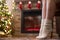 Bottom view of woman legs in knitted winter socks sitting on armchair near christmas tree and fireplace. Bottom view.