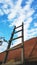 Bottom view of a wooden staircase set to the side of the roof against a blue cloudy sky, selective focus