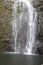 The bottom of Wailua Falls plummeting down a rocky cliff surrounded by lush vegetation in Hana, Maui