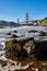 Boulders with crashing waves and seafoam along beach leading to Golden Gate Bridge