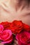 Bouquet of bright fresh red roses on the background of the female chest and collarbone