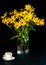 Bouquet of bright yellow flowers and white cup of coffee on black background. Jerusalem artichoke flowers in glass vase