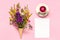 Bouquet colored wildflowers flowers in ice cream waffle cone, cup of tea and blank empty paper card for text on pink background