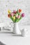Bouquet of colorful tulips, ceramic white teapot and teacup on the table in the bright kitchen. Cozy home concept