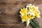 Bouquet of daffodils on wooden background, top view with space for text.