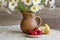 Bouquet of daisies in a clay jug and strawberries with pears