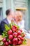 bouquet dark red burgundy peony with green leaves.guy with a girl in a white suit kiss on the background blurred.