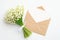 Bouquet of flowers lily of the valley and kraft paper envelope with blank note inside on white table. Romance, love letter,