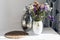 Bouquet of flowers, metal vase and straw wicker stand on the table, cozy home interior